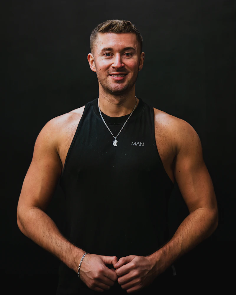 Coach souriant en débardeur noir dans une salle de sport